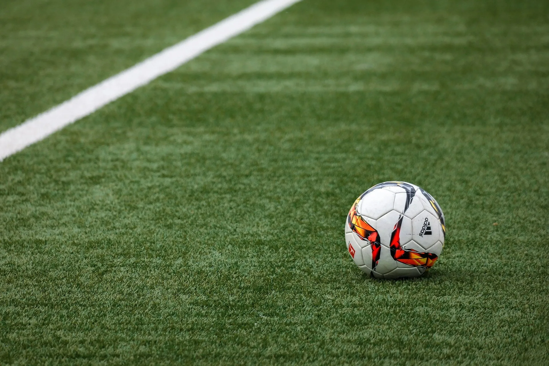 A soccer ball with a colorful design rests on vibrant artificial turf, near a white sideline.